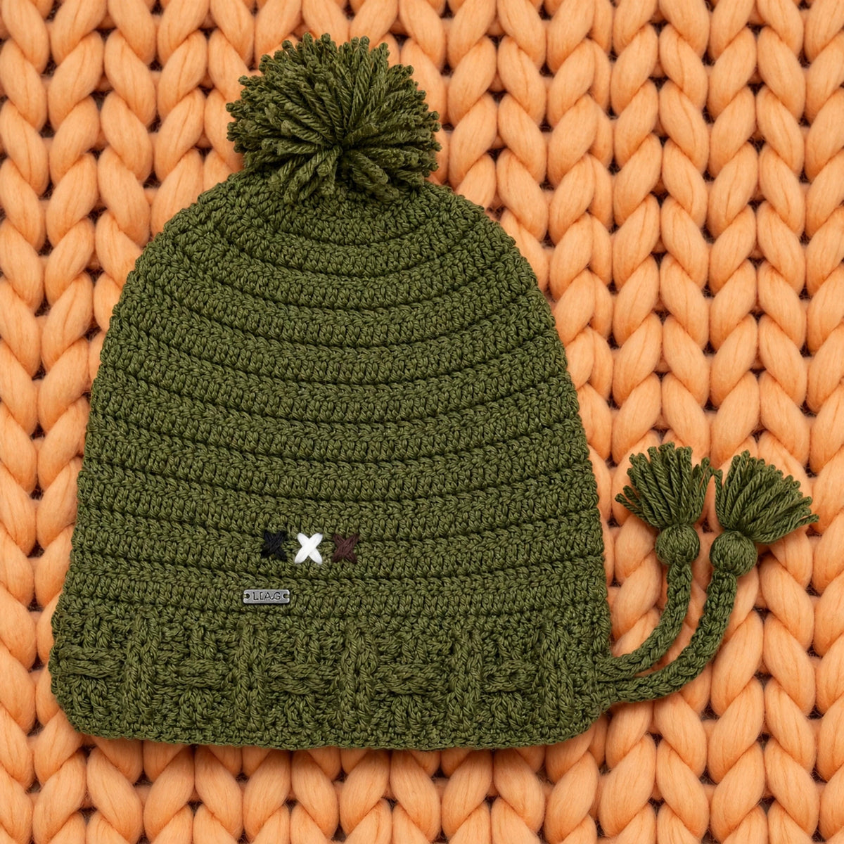 Vista completa gorro crochet verde oliva Olive Trail Pompom Edition con pompón y borlas laterales — LIA.G