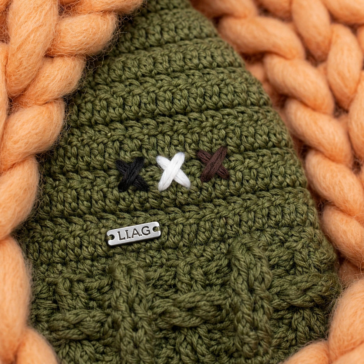 Detalle placa metálica LIA.G y bordado de aspas tricolor negro blanco marrón — Olive Trail Pompom