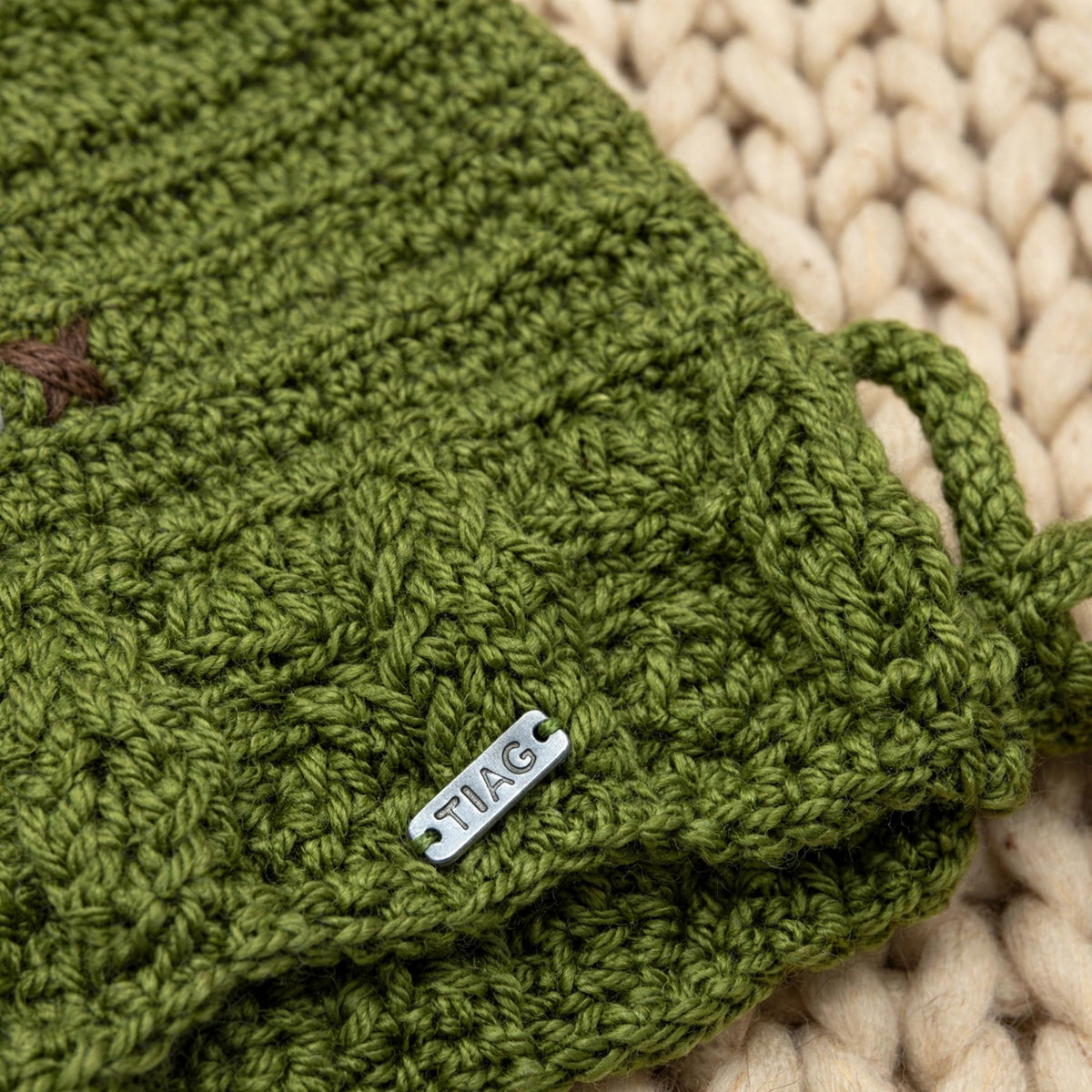 Detalle placa metálica LIA.G y textura punto cesta en puño inferior del gorro verde — Little Olive Elf LIA.G