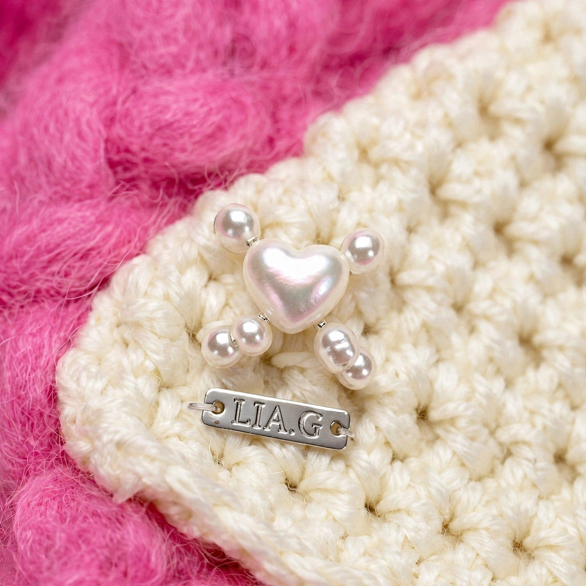 Detalle charm corazón perlado y cuentas sobre textura crochet granulada cruda con placa LIA.G — Ivory Heart