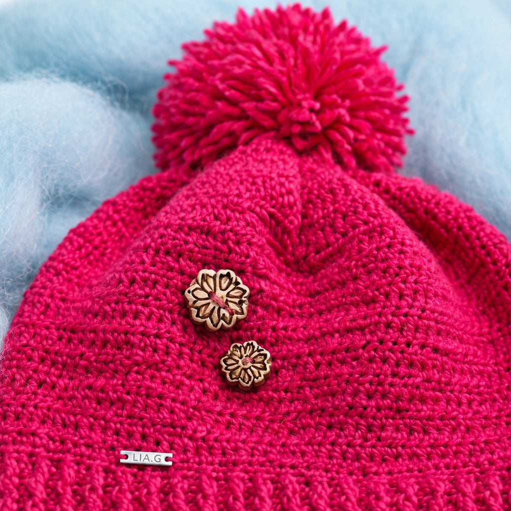 Detalle gorro fucsia con pompón y charms florales metálicos esmaltados rosa/dorado — Cherry Wrap LIA.G
