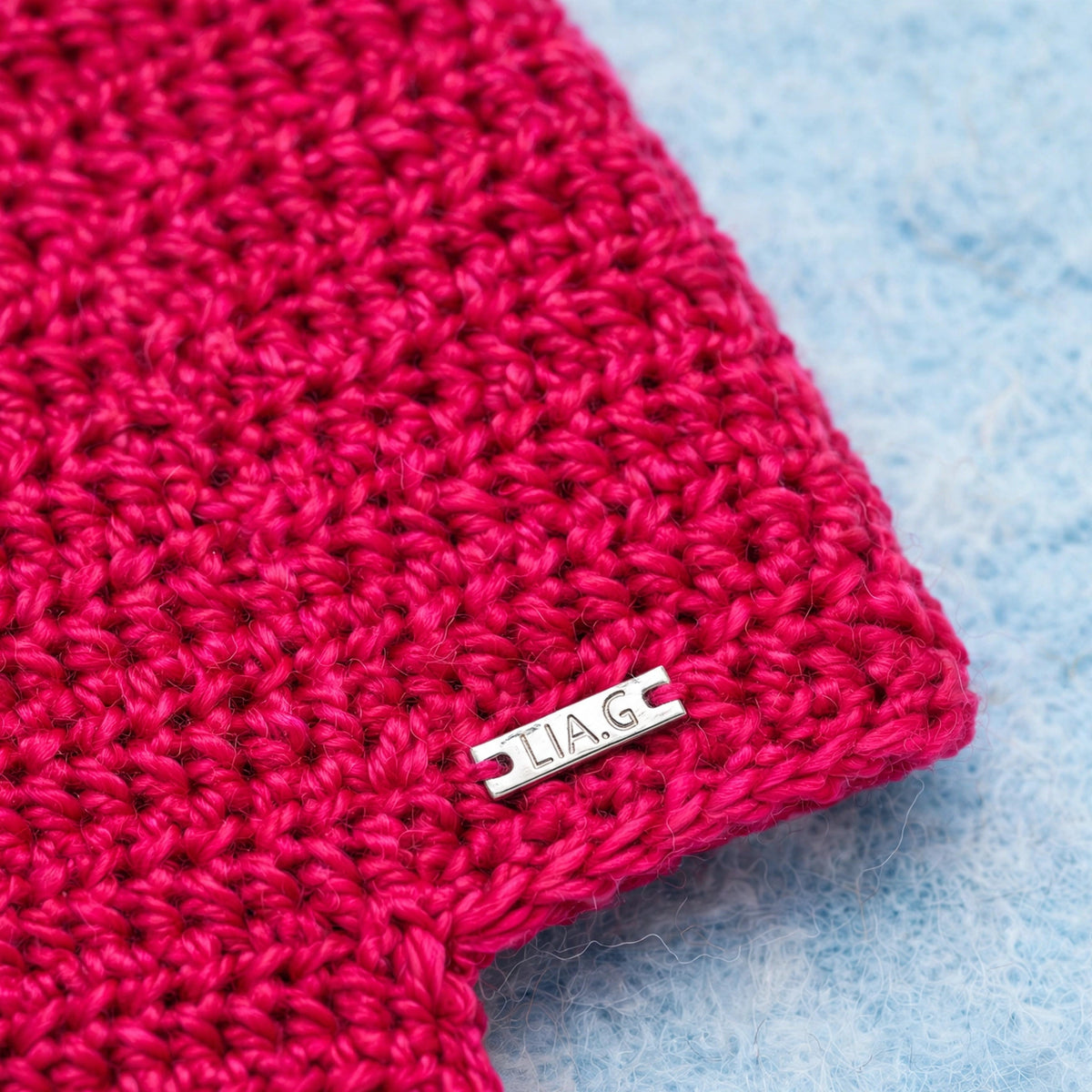 Detalle placa metálica LIA.G y textura punto bajo liso en bufanda fucsia — Cherry Wrap
