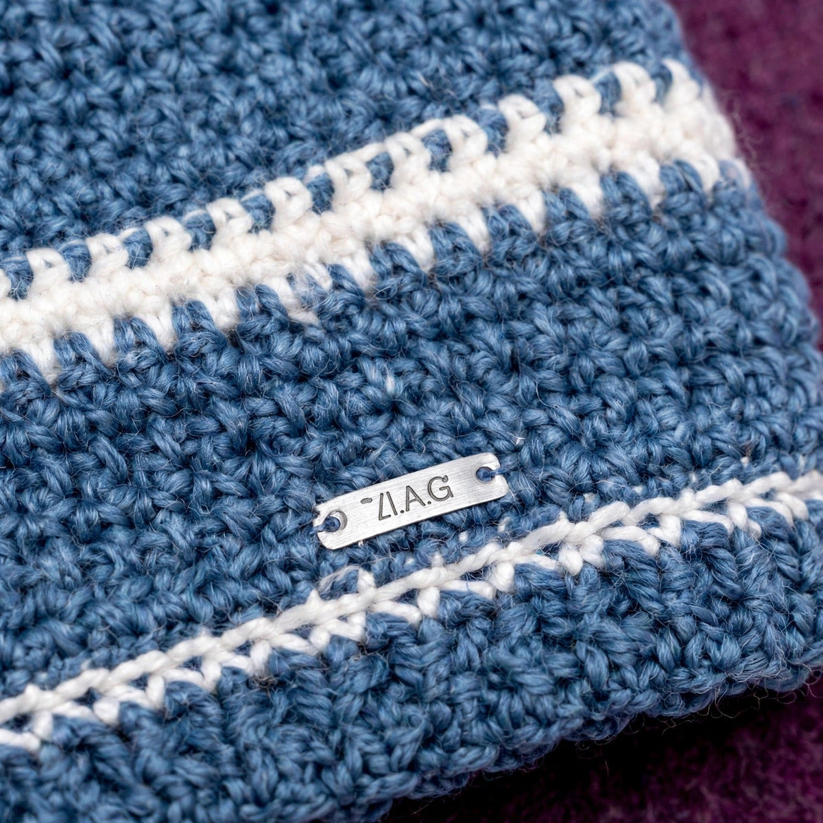 Detalle placa metálica LIA.G y raya fina crudo sobre fondo azul vaquero — Denim Wood LIA.G