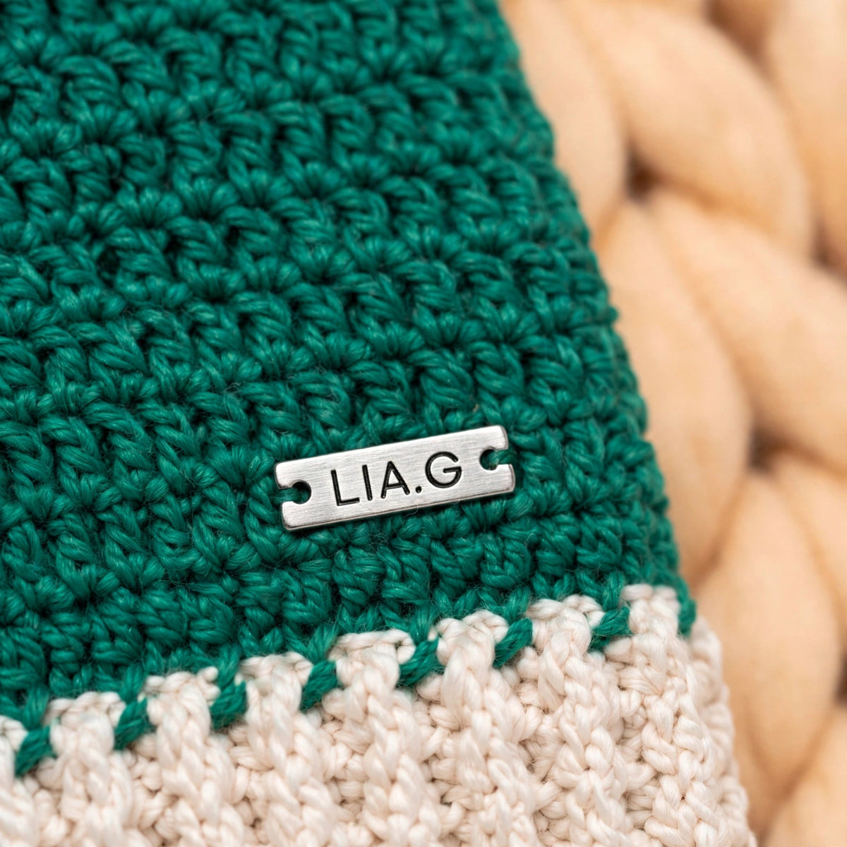 Detalle placa metálica LIA.G sobre banda crudo acanalada — Gorro Little Whiskers Verde