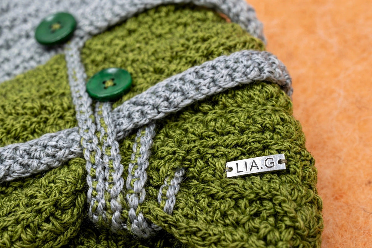 Detalle correa gris tejida con placa metálica LIA.G y 2 botones verdes funcionales sobre cuerpo verde musgo — Moss Buckle
