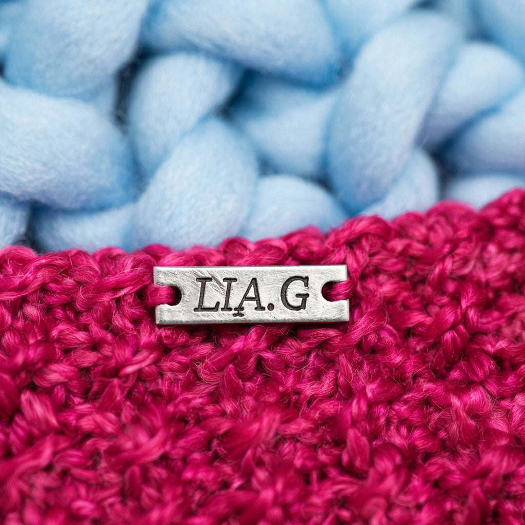 Detalle placa metálica LIA.G sobre textura punto musgo fucsia — Little Whiskers Baby Pink LIA.G