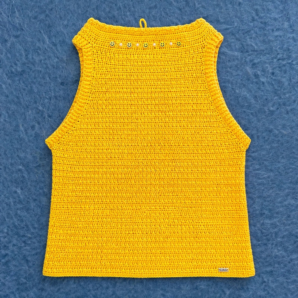 Vista completa del top crochet halter amarillo sobre fondo de lana azul — LIA.G